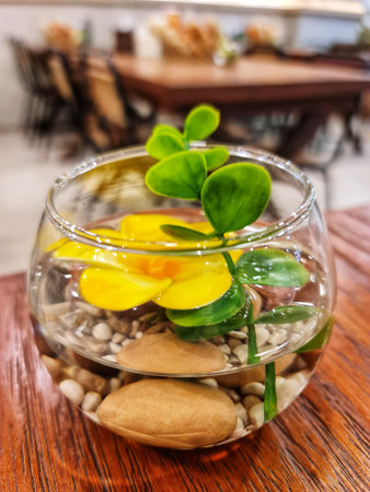 Glass bowl containing water, stones, a yellow flower and a green plant makes a table centerpiece Perfect for interior decoration.の写真素材