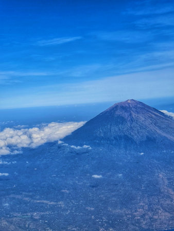 Aerial shot of Mount Agung in Bali under a blue sky with scattered clouds, creating a serene yet stunning landscape view Perfect for travel and adventure themes.の写真素材