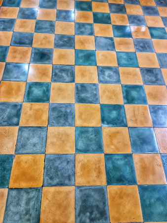 Eye-level view of a checkered floor with old blue and gold square tiles creating a geometric pattern...