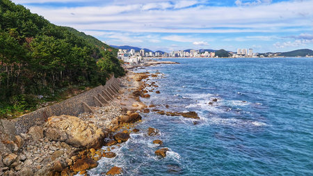Scenic coastal view featuring a rocky shoreline merging with a deep blue ocean and a distant city...