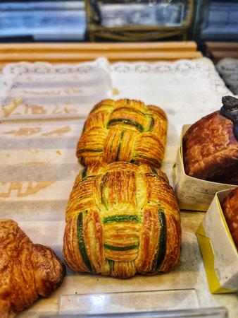 A selection of freshly baked pastries, including braided breads and croissants, are arranged in a bakery window display offering a tempting treat.の写真素材