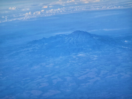 Expansive aerial shot reveals a mountain range beneath a cloudy blue sky creating a scenic travel vista Useful for travel and nature related content.の写真素材