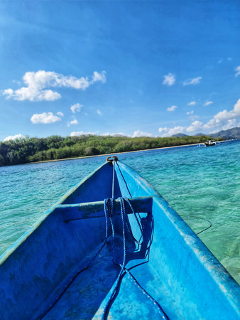 Blue boat floats on clear turquoise water towards a tropical island under a bright blue sky Perfect for travel and summer vacation themes.の写真素材