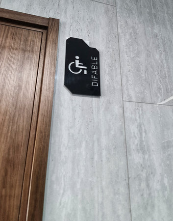 Black accessible restroom sign mounted on wall next to a wooden door indicates inclusion for differently abled individuals for inclusive architecture projects.の写真素材