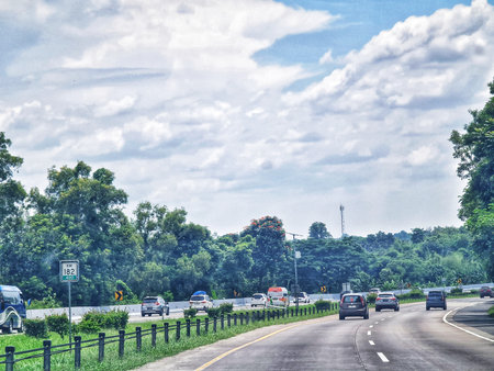 Palimanan, Indonesia on 6 April 2025. Cars drive on a highway with a cloudy sky and green trees alongside the road, creating a peaceful and natural scene for travel and transportation concepts.の写真素材