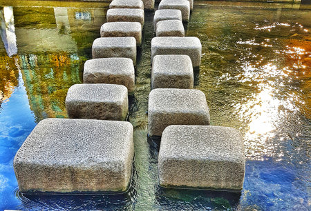 Stone path over gently flowing water creates a peaceful scene with sunlit reflections great for meditation or travel themed projects.の写真素材