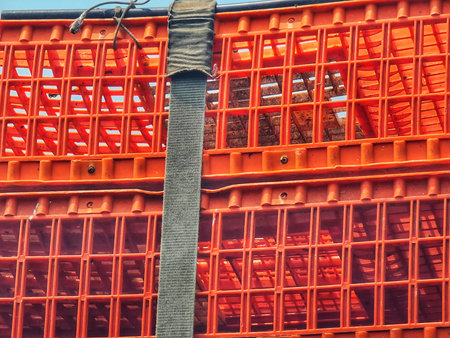 Stacked orange plastic crates are secured with a gray strap against a bright blue sky, creating a structured and industrial aesthetic, ideal for use in transportation or storage marketing.の写真素材