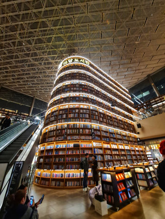 Seoul, South Korea on 7 Nov 2024. Grand bookshelf structure glows under a high, industrial ceiling as people browse in a modern interior space, perfect for library or architectural concepts.のeditorial素材