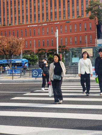 Seoul, South Korea on 10 Nov 2024. Mature asian woman crossing street on crosswalk with other people in sunlit urban setting, creating pedestrian scene for lifestyle or travel advertisements.のeditorial素材