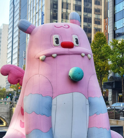 Seoul, South Korea on 11 Nov 2024. Pink cartoon monster sculpture stands tall in urban cityscape with surrounding buildings, creating whimsical mood, ideal for children's content and creative marketing campaigns.のeditorial素材
