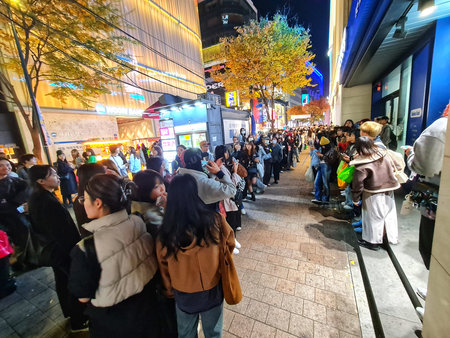 Seoul, South Korea on 11 Nov 2024. Large crowd standing in long line on an illuminated city street...