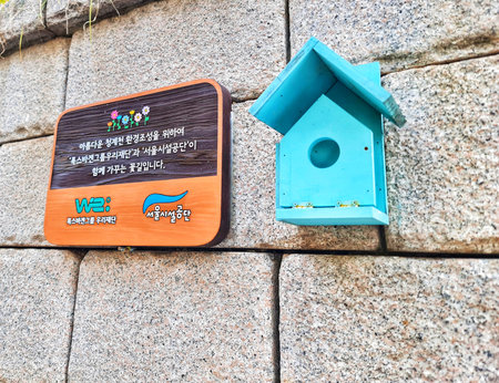 Seoul, South Korea on 11 Nov 2024. Small, bright turquoise birdhouse with a pitched roof is mounted on a textured stone wall next to a decorative sign, creating a charming outdoor scene suitable for nature and DIY projects.のeditorial素材