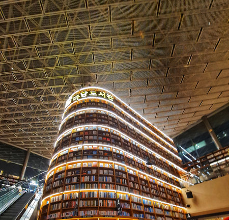 Seoul, South Korea on 7 Nov 2024. Large bookcase filled with books is centered in a public library with a high metal ceiling and is lit by warm lights, creating a modern and academic atmosphere suitable for educational or architectural publications.のeditorial素材