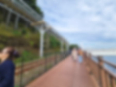 A blurred figure walks along a wooden ocean walkway with green hillside under a cloudy sky, creating...