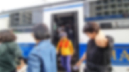 Blurred figures are boarding a white bus with blue accents in bright daylight, creating a sense of...