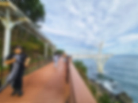 Blurred pedestrian walkway with tan railing runs alongside ocean with a white bridge in the...