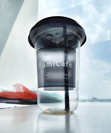 Jakarta, Indonesia on 29 Oct 2025. Clear plastic cup with a dark lid and straw sits on a bright table near a window showing sky, perfect for illustrating drinks and cafe style.のeditorial素材