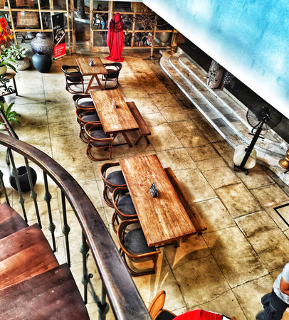 Bogor, Indonesia on 25 Oct 2025. Elevated perspective reveals inviting restaurant interior featuring wooden tables, chairs, and staircase under natural lighting, creating a warm and rustic atmosphere ideal for food and travel-related marketing.のeditorial素材