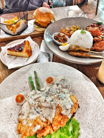 Bogor, Indonesia on 25 Oct 2025. Varied food plates with burger, chicken, rice and dessert on wooden table are shot with natural lighting, creating inviting atmosphere perfect for restaurant and lifestyle marketing.のeditorial素材