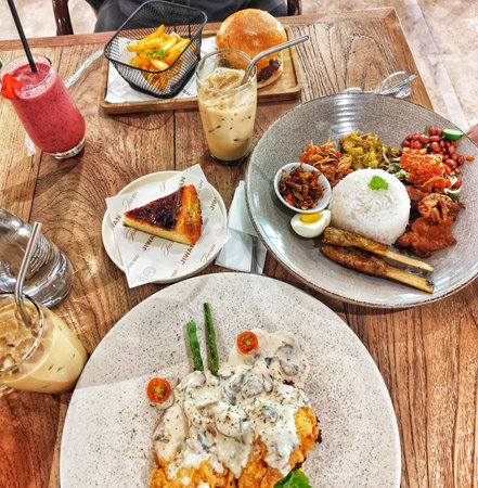 Bogor, Indonesia on 25 Oct 2025. Overhead shot showcases assorted food dishes like burger, fries, cake, rice, iced drinks on a wooden table, presenting a diverse culinary experience with warm lighting, perfect for restaurant and food blog content.のeditorial素材