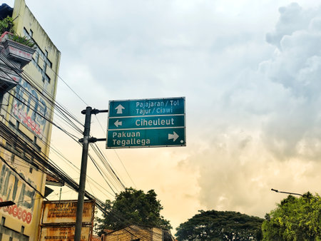 Bogor, Indonesia on 25 Oct 2025. Green directional signs stand against a cloudy sky in an urban city, indicating various road destinations, providing a visual for travel or wayfinding concepts.のeditorial素材