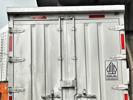 Cikarang, Indonesia on 30 Oct 2025. A sturdy gray metal industrial door is displayed with vertical panels, hinges, reflectors and locking mechanisms, set against an urban cityscape, suitable for logistics or transportation themed marketing.のeditorial素材