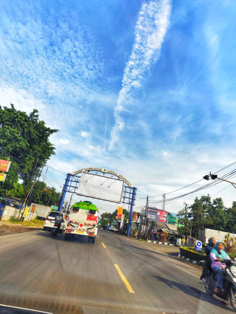 Cikampek, Indonesia on 20 nov 2025. Street view shows highway leading to city entrance, featuring vehicles, a bright blue sky with white clouds, and lush green trees, perfect for transportation and travel editorials.のeditorial素材