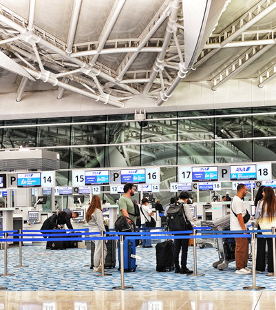 Tokyo, Japan on 20 Oct 2025. Haneda Airport. Diverse group of travelers with luggage waiting at modern airport check-in counters, some wearing masks, conveying a sense of anticipation under bright, airy lighting ideal for travel or lifestyle content.のeditorial素材