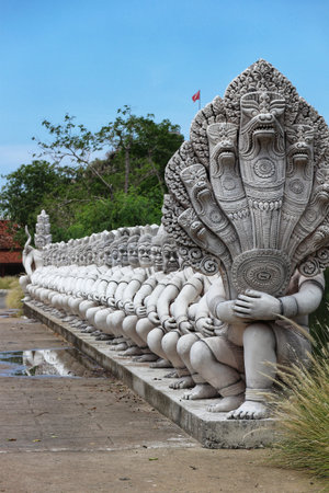 Bangkok, Thailand on 25 July 2023. Stone Naga statues are squatting in a repetitive row under a partly cloudy sky, exhibiting cultural heritage and historic architecture suitable for tourism or Southeast Asia themes.のeditorial素材
