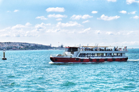 Istanbul, Turkey on 12 July 2022. Passenger ferry navigates through open waters under a bright cloudy sky with a distant cityscape viewable, perfect for travel and recreational themes.のeditorial素材