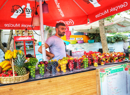 Istanbul, Turkey on 12 July 2022. A man stands behind a stall filled with colorful fruit cups and fresh produce, ready to serve customers a healthy treat Perfect for food and travel related projects.のeditorial素材
