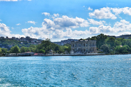 Istanbul, Turkey on 12 July 2022. A stately mansion sits along a waterfront with a backdrop of trees and a partly cloudy sky, creating a peaceful and scenic view for travel or architectural projects.のeditorial素材