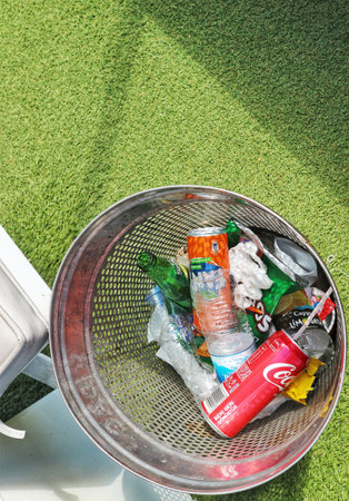 Istanbul, Turkey on 12 July 2022. Metal mesh trash bin filled with various waste items is placed on green artificial turf. This image depicts waste management and disposal concepts.のeditorial素材