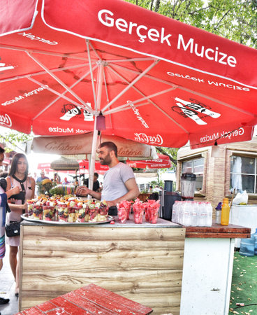 Istanbul, Turkey on 12 July 2022. A vendor stands behind his stall selling fresh fruit cups in a vibrant outdoor market setting Perfect for illustrating street food or summer travel.のeditorial素材
