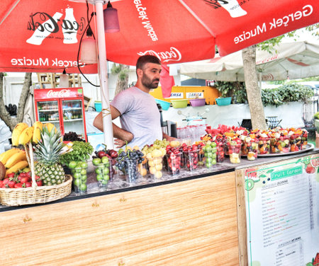 Istanbul, Turkey on 12 July 2022. A man stands behind a fruit stand displaying an assortment of fruit cups and fresh produce Perfect for food market and street vendor related content.のeditorial素材