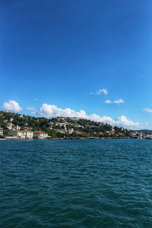 Scenic view of a coastline featuring a hillside with homes and buildings, captured under a bright, cloud-dotted sky, ideal for showcasing coastal landscapes or travel destinations.のeditorial素材