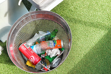 Istanbul, Turkey on 12 July 2022. A metal trash can is overflowing with plastic bottles and cans on a green lawn, illustrating waste management for environmental awareness projects.のeditorial素材
