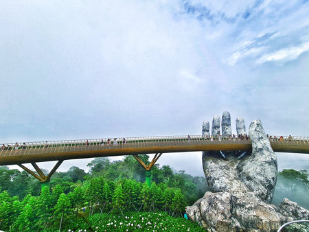 Da Nang, Vietnam on 13 May 2025. Ba Na Hills. People enjoy walking on a unique bridge structure supported by a giant stone hand, surrounded by lush green foliage and misty skies, perfect for travel blogs.のeditorial素材