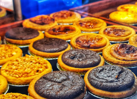 A variety of golden egg tarts and rich chocolate tarts fill a bakery display case for sale Perfect for illustrating dessert or food concepts.の写真素材