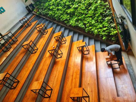 Jakarta, Indonesia on 1 Jun 2025. A person arranges small tables with a geometric design along wooden steps, accompanied by a vibrant green wall, creating an interesting modern atmosphere Perfect for showcasing innovative designs.のeditorial素材