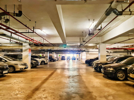 Bekasi, Indonesia on 12 Jun 2025. Several parked cars fill an underground parking garage with visible pipes and ceiling details, suitable for urban planning or architectural projects.のeditorial素材