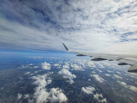 A breathtaking aerial view from an airplane window showcases a vast expanse of fluffy white clouds...