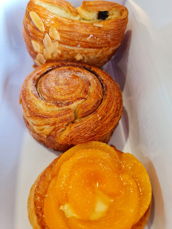 Three delicious pastries are displayed in a white container.  The top pastry features almonds, the...