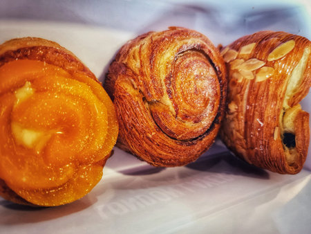 Three delectable pastries are showcased in a close-up shot.  A vibrant orange-filled pastry sits...