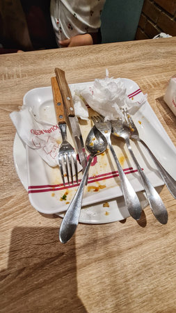 Jakarta, Indonesia on 4 Jan 2024. a used plate and cutlery on a wooden table in a restaurant setting. The plate shows remnants of a meal, and the utensils are haphazardly placed nearby. The overall impression suggests a finished meal.のeditorial素材