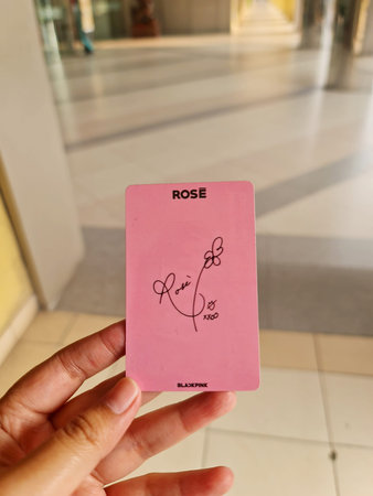 Bekasi, Indonesia on 24 Aug 2024. A close-up image shows a hand holding a pink card featuring Rose's autograph. The card has her name, signature, a small flower design, and 'Blackpink' printed at the bottom. The background is a blurred indoor setting.のeditorial素材