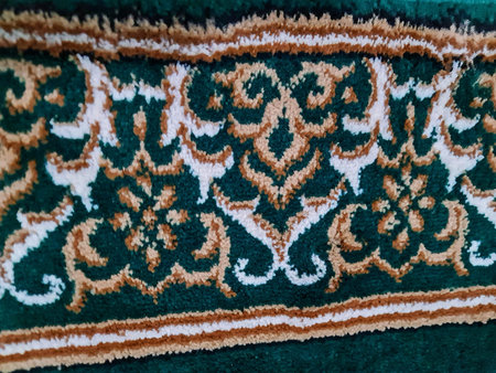 Close-up view of a green carpet section showcasing an intricate floral pattern. The design incorporates beige and white accents creating a detailed and elegant look. The texture appears soft and plush.のeditorial素材