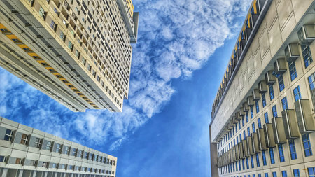 Bekasi, Indonesia on 1 Feb 2024. Three modern apartment buildings viewed from below against a vibrant blue sky with fluffy white clouds. The image emphasizes the buildings' height and the contrast between architecture and nature. The perspective creates aのeditorial素材