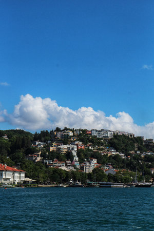Istanbul, Turkey on 12 July 2022. Scenic coastal homes cascade down a green hillside, viewed from the sea under a bright blue sky, which is perfect for travel inspiration.のeditorial素材