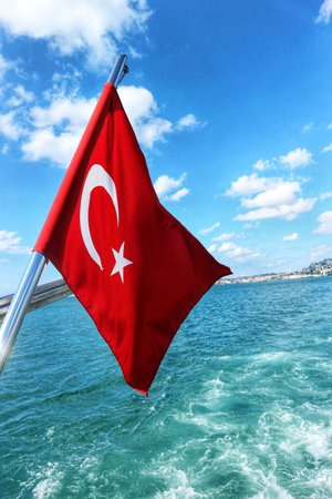 Istanbul, Turkey on 12 July 2022. Bosphorus. Red flag with white crescent and star flies on a boat with the ocean and blue sky behind it, creating a sense of freedom Perfect for travel-related imagery.の写真素材